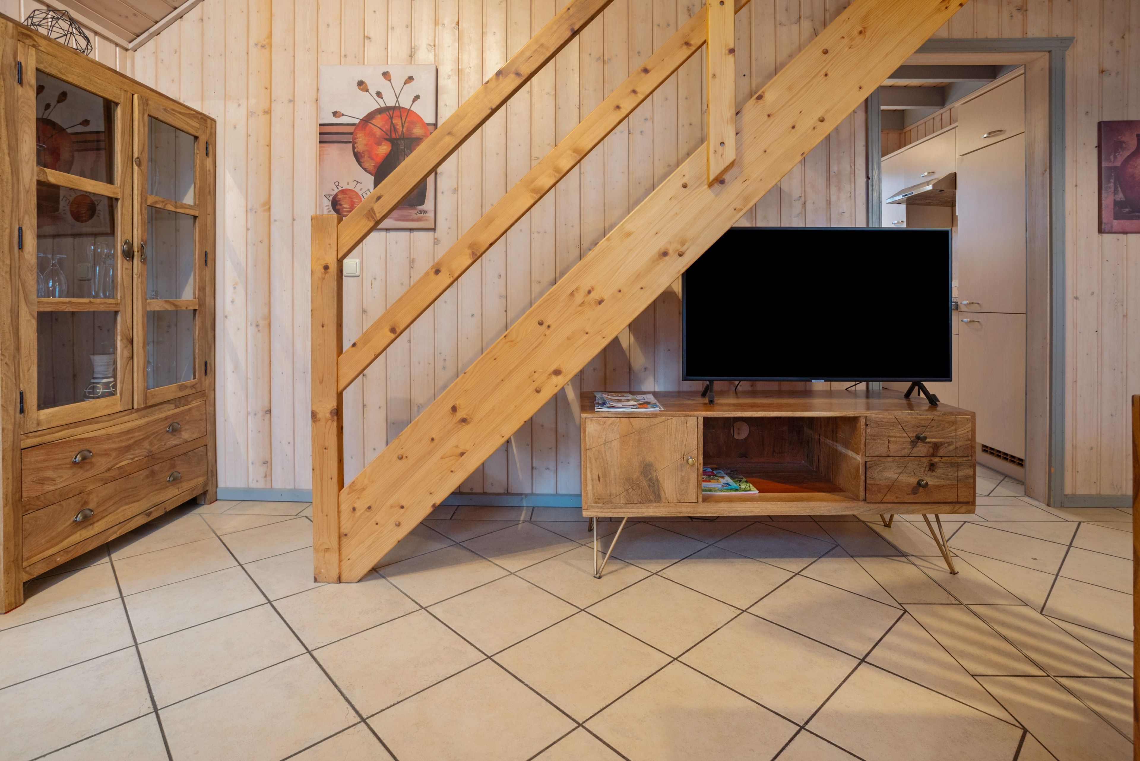 Un escalier en bois menant à un deuxième étage, un meuble en bois avec des portes en verre et un téléviseur posé sur un meuble en bois.