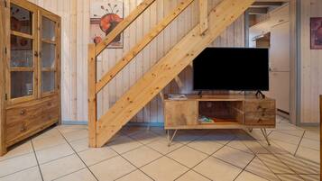 Un escalier en bois menant à un deuxième étage, un meuble en bois avec des portes en verre et un téléviseur posé sur un meuble en bois.