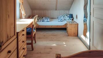 A compact room with a wooden desk, a single bed with patterned bedding, and a small bedside table with a lamp.