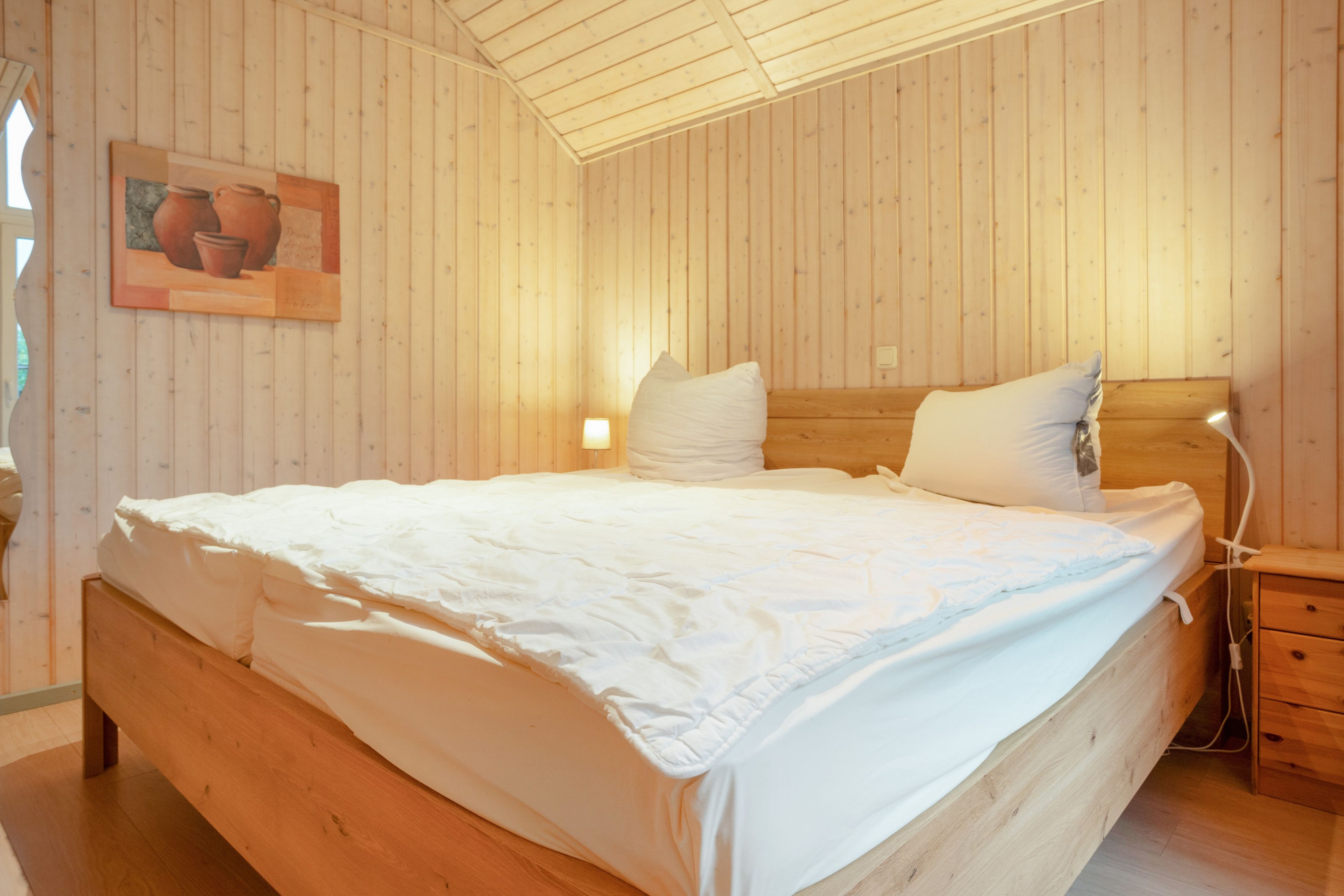 A wooden room with a bed, a nightstand, and a wall-mounted lamp.