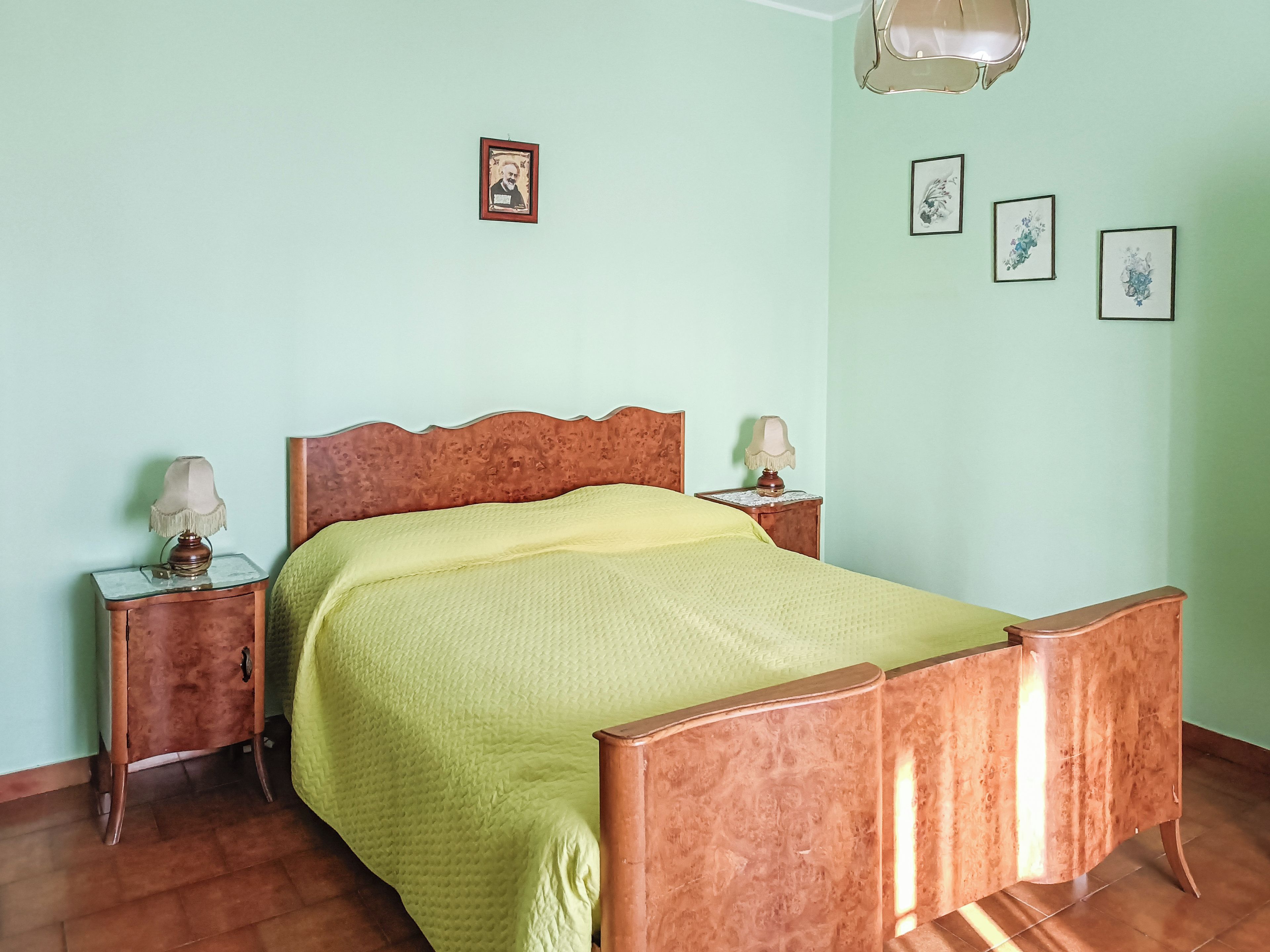 A room with a bed, two bedside tables with lamps, a wall with framed pictures, and a wooden floor.