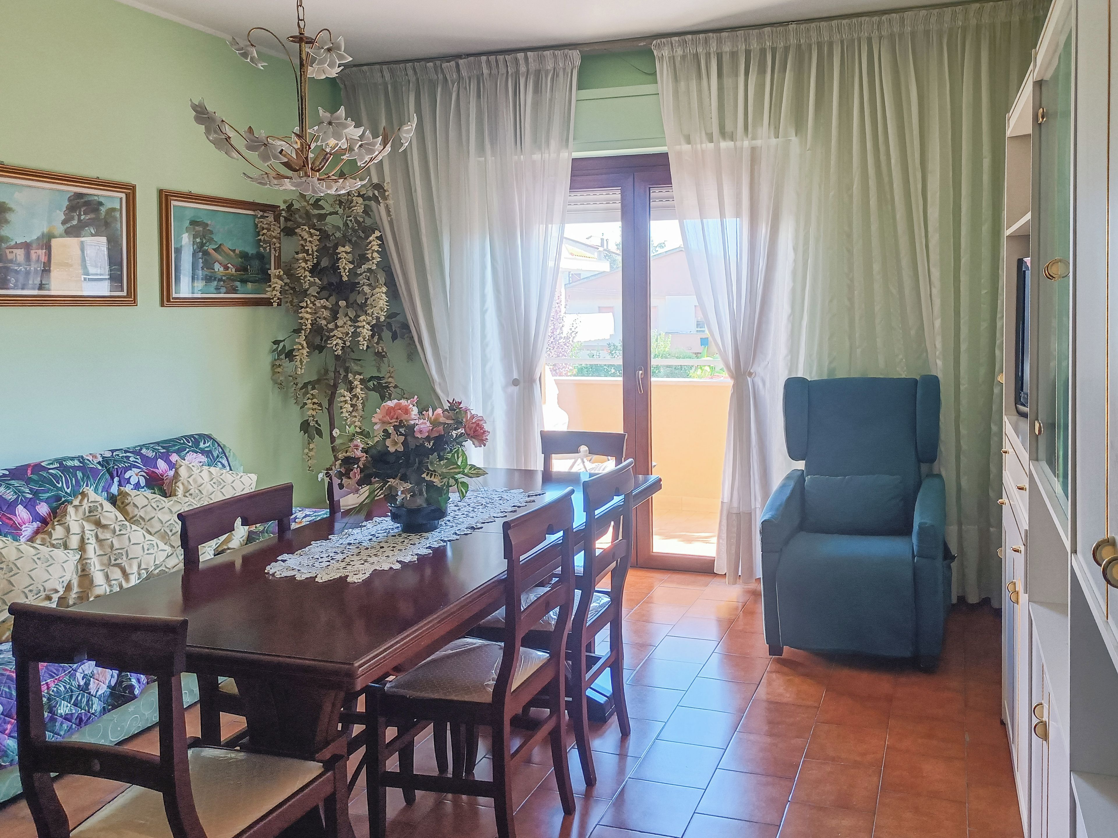 A dining area with a table, chairs, a vase of flowers, and a view through a glass door to an outdoor balcony.