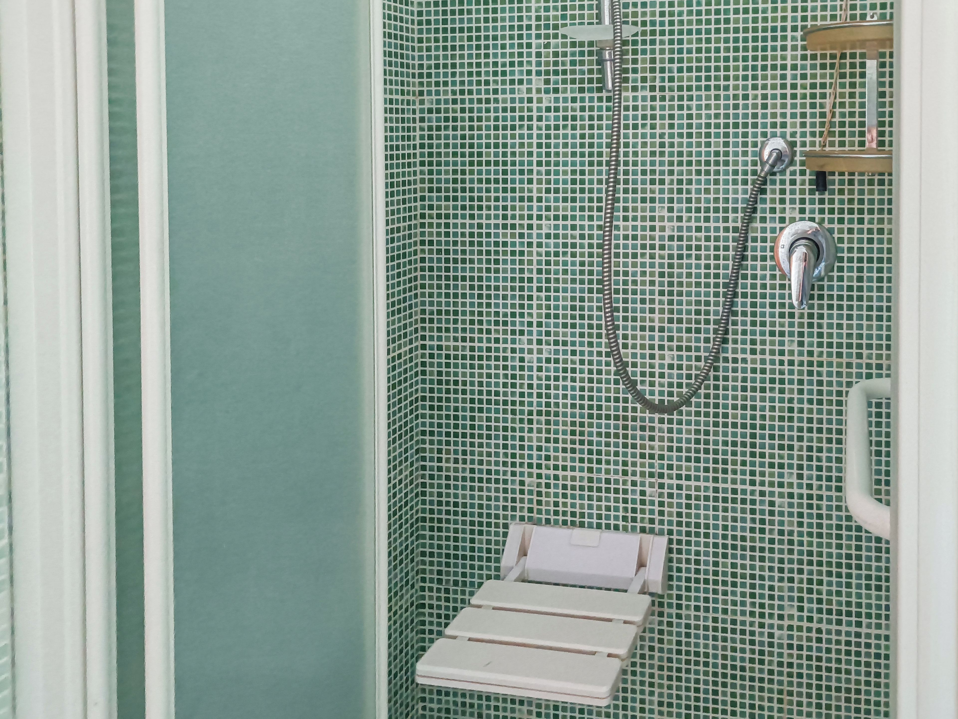 Un espace douche avec un mur carrelé, une pomme de douche et un porte-serviettes blanc.