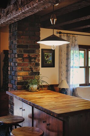 Un espace bar avec un comptoir en bois, des tabourets, un luminaire suspendu et un mur en briques.