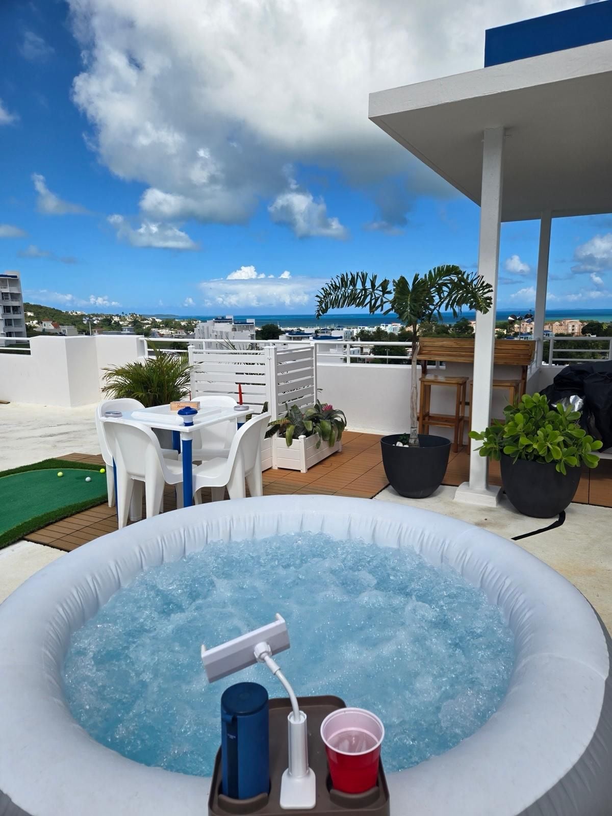An outdoor hot tub with a view of the sea, a table with chairs, and potted plants.