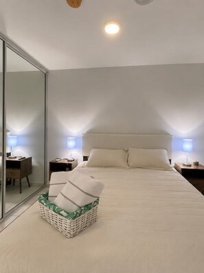 A bedroom with a large bed, bedside tables with lamps, a mirror, and a wicker chair. - Traducción (Ceiba)