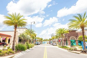 A street lined with palm trees and buildings, including a stop sign and a blue storefront. - Azure Escape Cottage | Hot Tub + Margaritaville & Waterpark Access - 3058PI (Kissimmee)