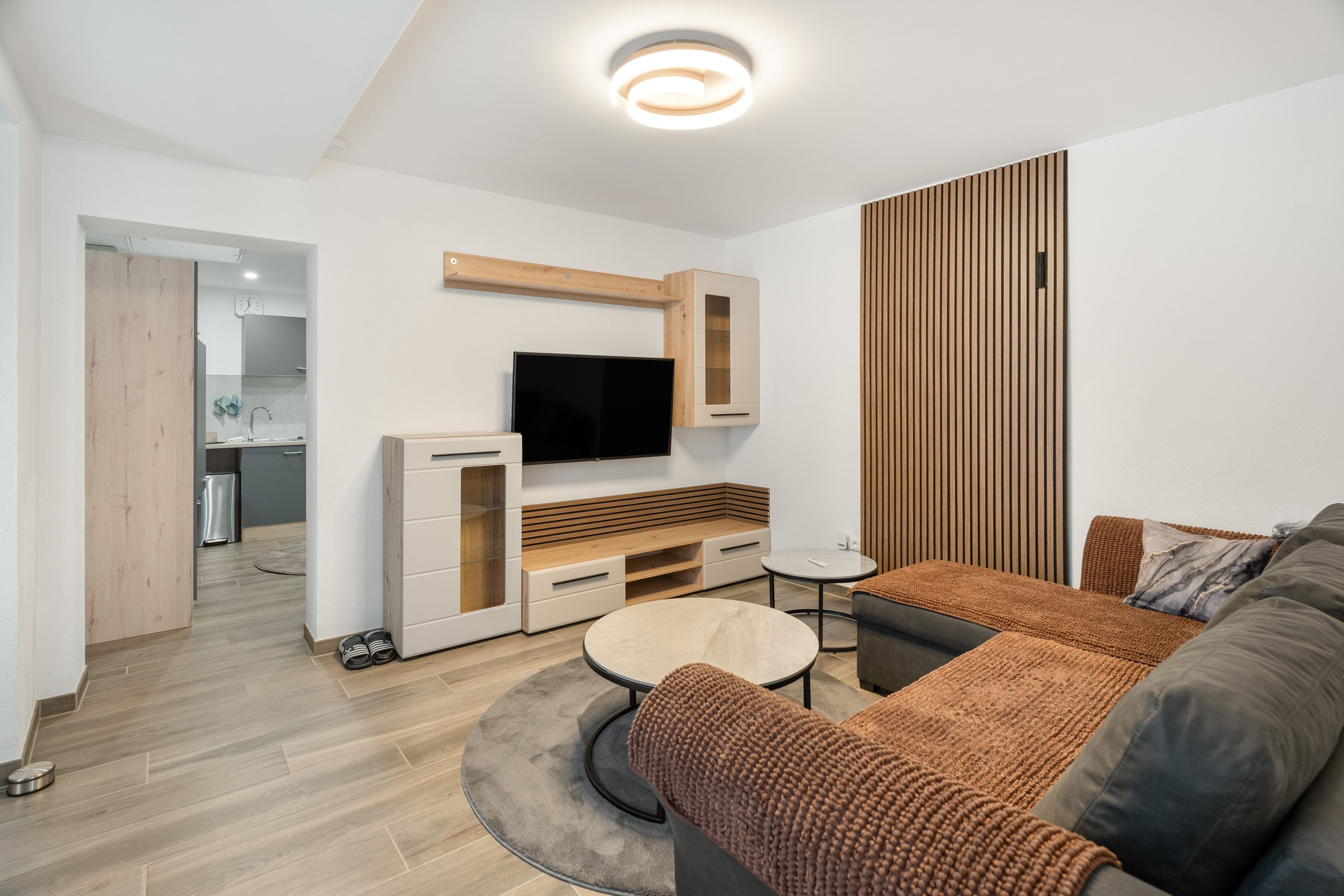Un salon moderne avec un téléviseur à écran plat fixé sur un panneau en bois, un canapé, une table basse et une petite table d’appoint.