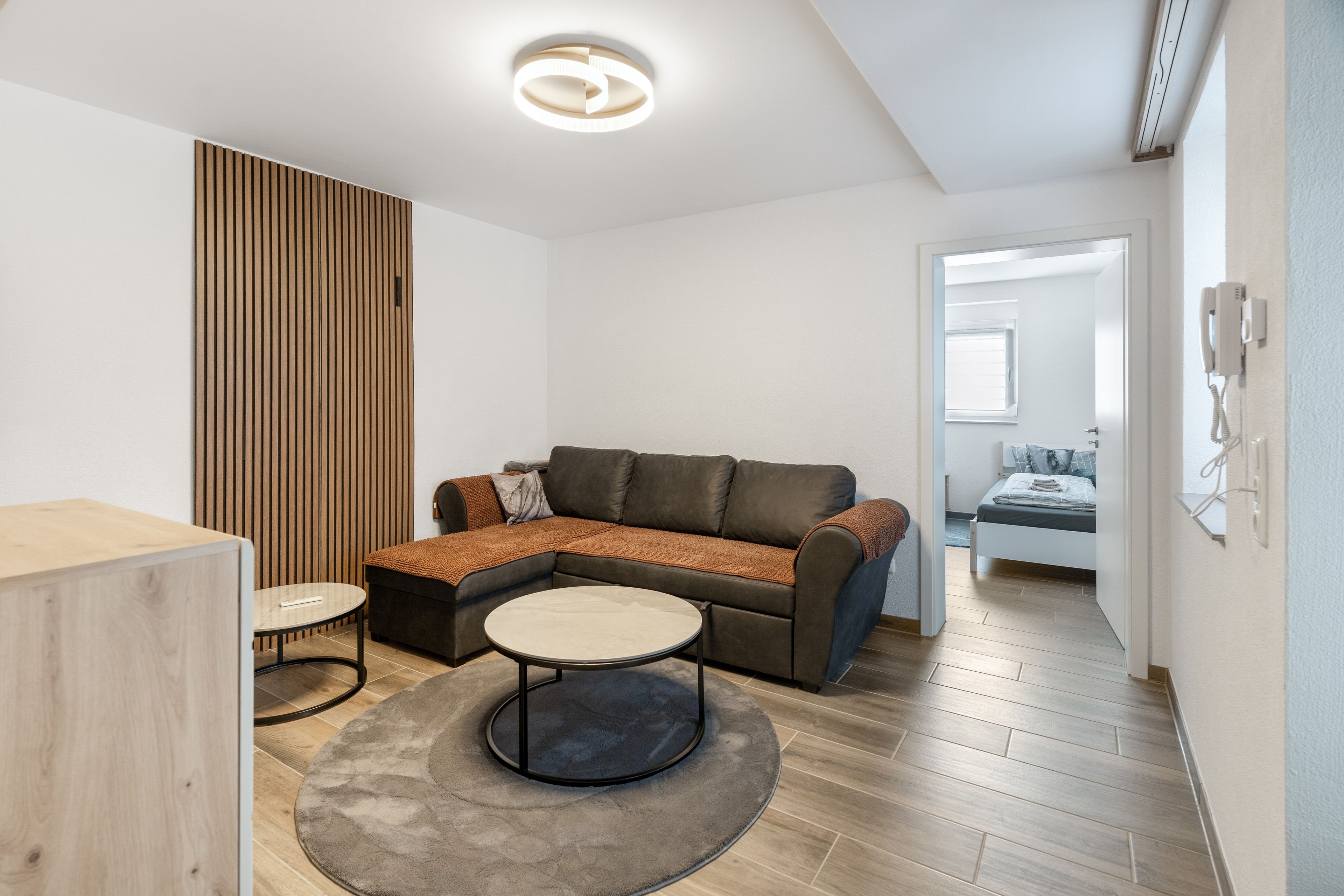 Ein modernes Wohnzimmer mit einer Eckcouch, einem runden Couchtisch und einer Wand mit Holzvertäfelung.