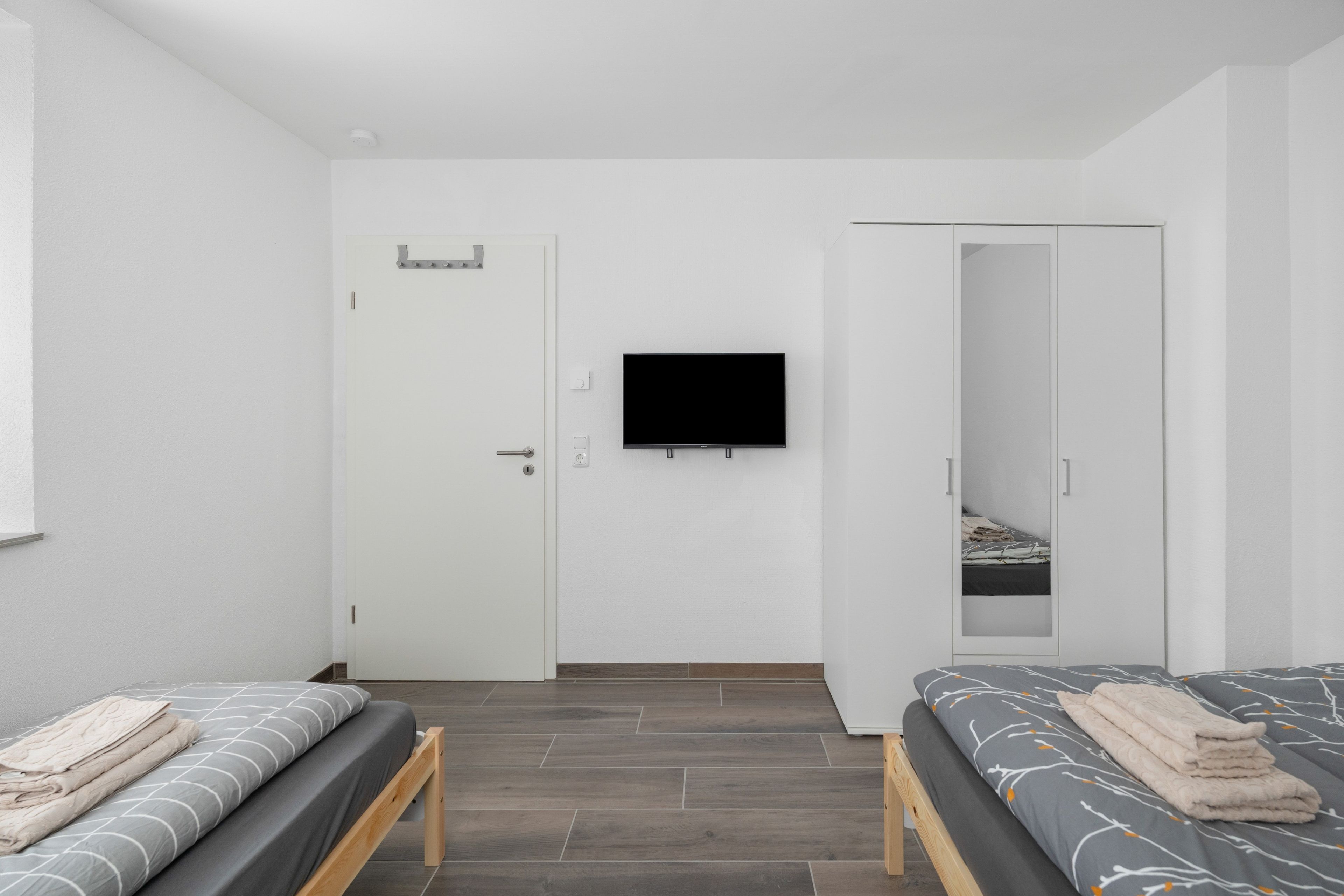 Ein Zimmer mit zwei Betten, einem Fernsehgerät an der Wand und einem Kleiderschrank.