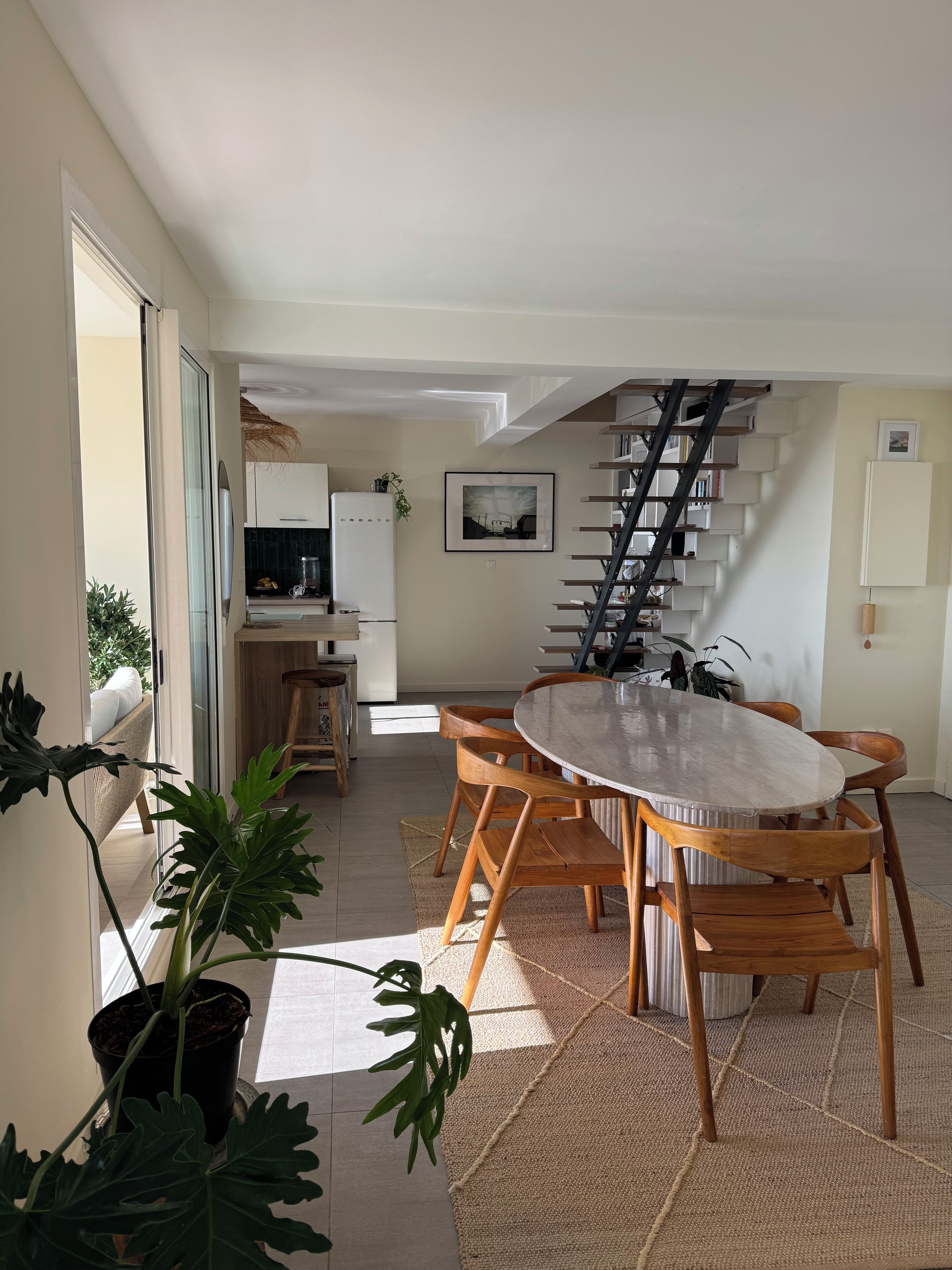 Une cuisine moderne avec des meubles blancs, un réfrigérateur et un coin repas comprenant une table ronde et des chaises en bois.