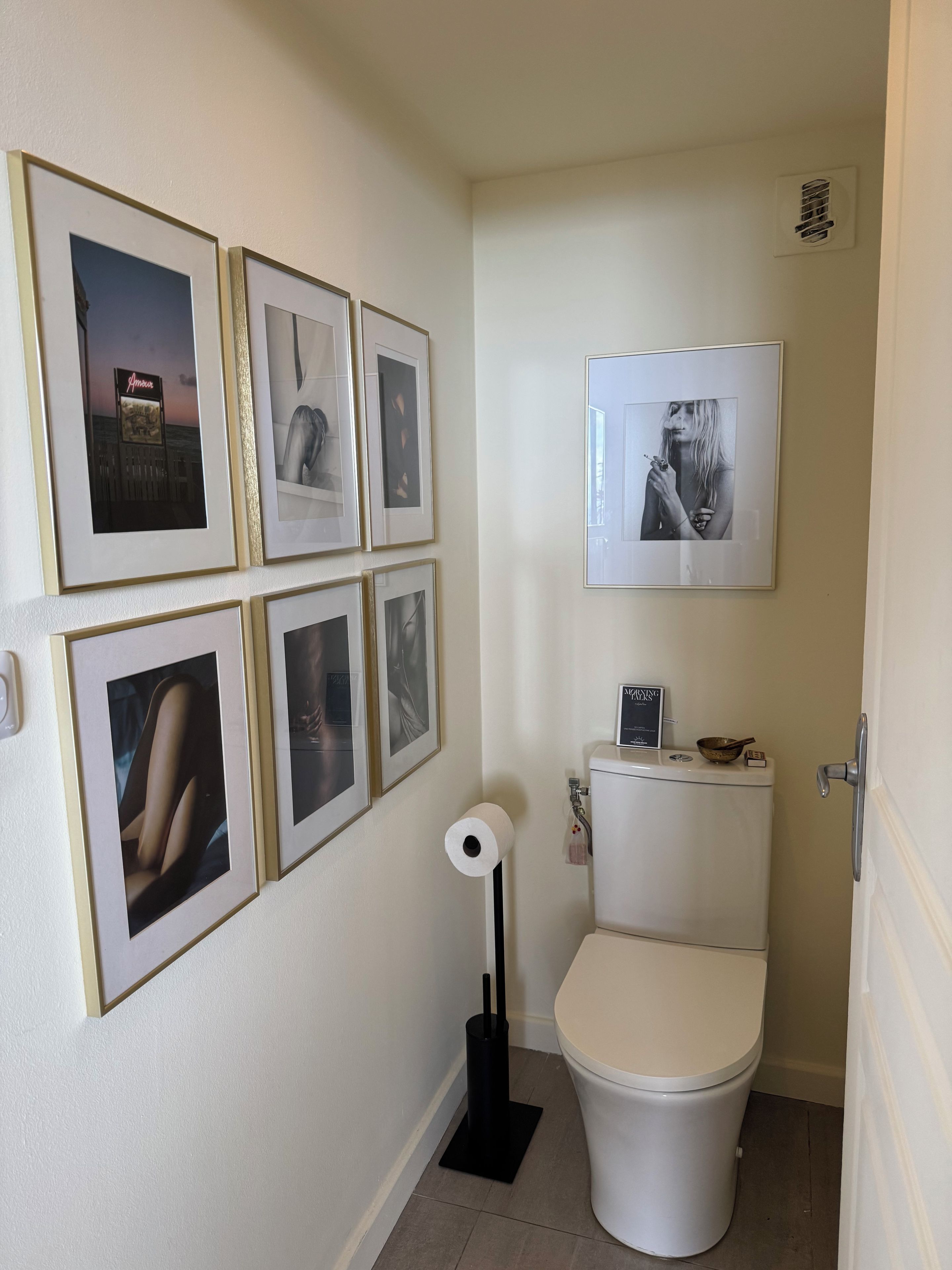 Une salle de bain avec des toilettes, un rouleau de papier toilette et six tableaux encadrés accrochés au mur.