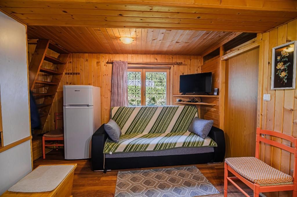 Un interior de cabaña acogedor con sofá, televisor, refrigerador y escalera de madera.