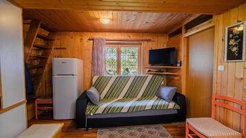 Un interior de cabaña acogedor con sofá, televisor, refrigerador y escalera de madera.