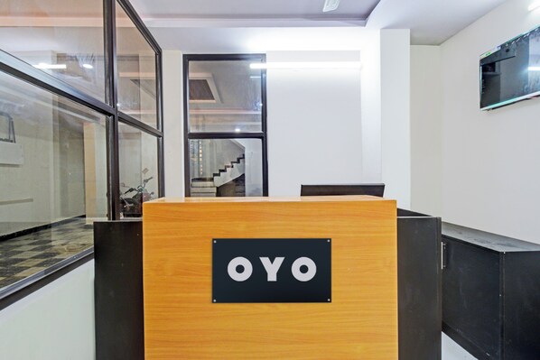 Balcão de recepção com uma placa que diz 'OYO', em um interior moderno com paredes de vidro e uma escada ao fundo.