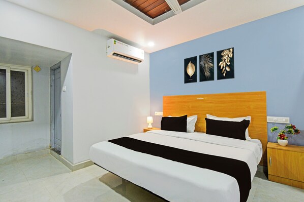 A bedroom with a bed, a nightstand, a wall-mounted air conditioner, and three framed wall decorations.