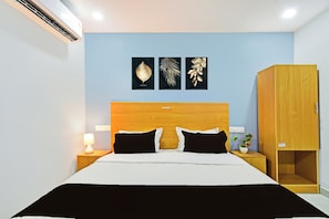Quarto de hotel com cama, mesas de cabeceira, abajur, guarda-roupa e obras de arte nas paredes.
