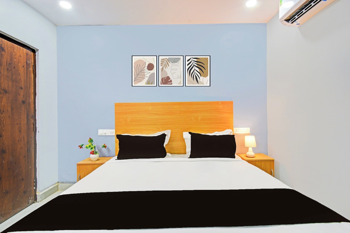 Quarto com cabeceira de madeira, cama com roupa de cama preta e branca, duas mesas de cabeceira com abajures e três obras de arte penduradas na parede.