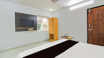 Un dormitorio con cama, televisor, armario de madera, una mesita con hervidor y una puerta.