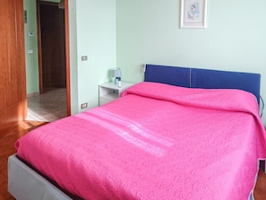 A bedroom with a bed, a nightstand, a lamp, and a door leading to another room. - Orchidea - Spacious Apartment in Spoltore (Santa Teresa)