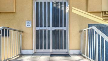 A building entrance with a glass door, metal railings, and a tiled ground.