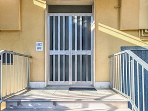 A building entrance with a glass door, metal railings, and a tiled ground. - Orchidea - Spacious Apartment in Spoltore (Santa Teresa)