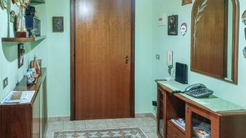A room with a wooden door, a desk with papers, a telephone, a mirror, and a shelf with various items.
