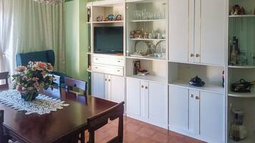 A dining area with a wooden table, chairs, a vase of flowers, a chandelier, and a white cabinet with glass doors.