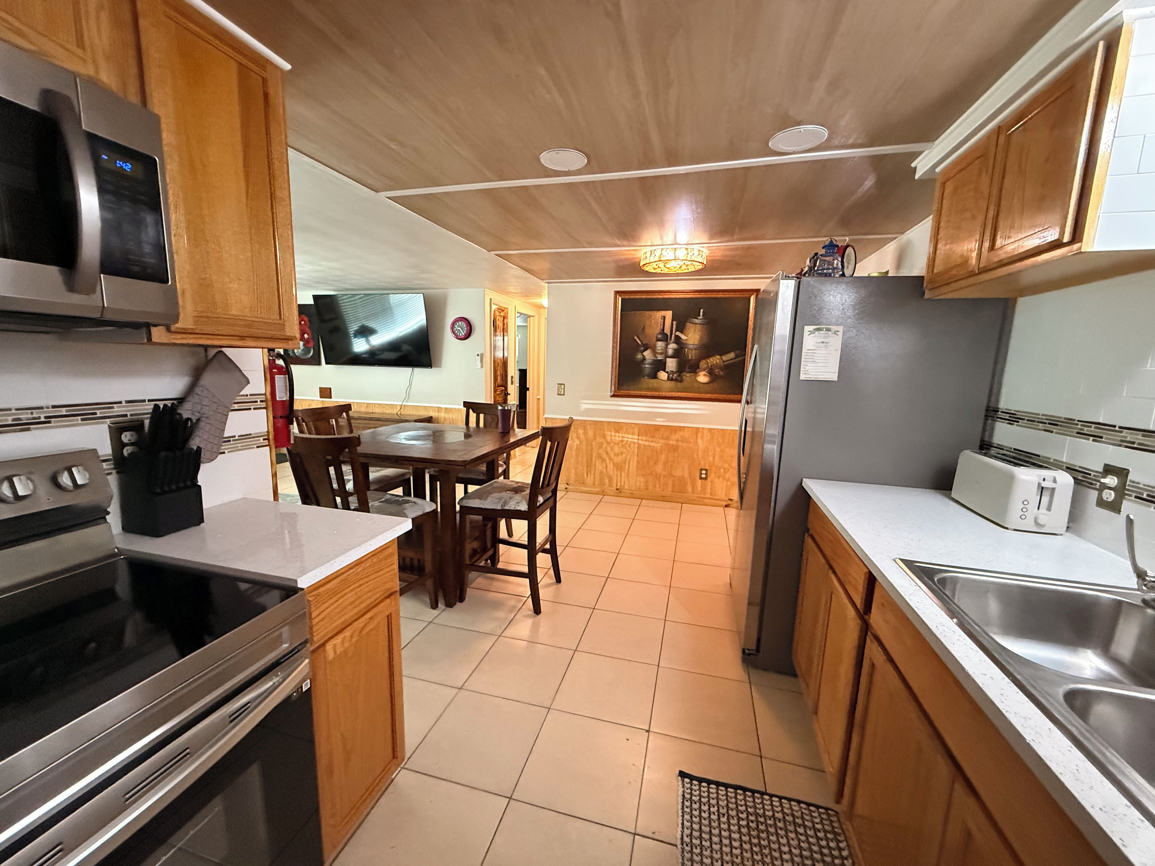 A kitchen with wooden cabinets, a stainless steel refrigerator, a microwave, and a dining area with a table and chairs.