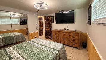 A bedroom with two beds, a wooden dresser, a television, and a ceiling fan.