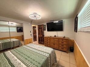 Un dormitorio con dos camas, un aparador de madera, un televisor y un ventilador de techo.