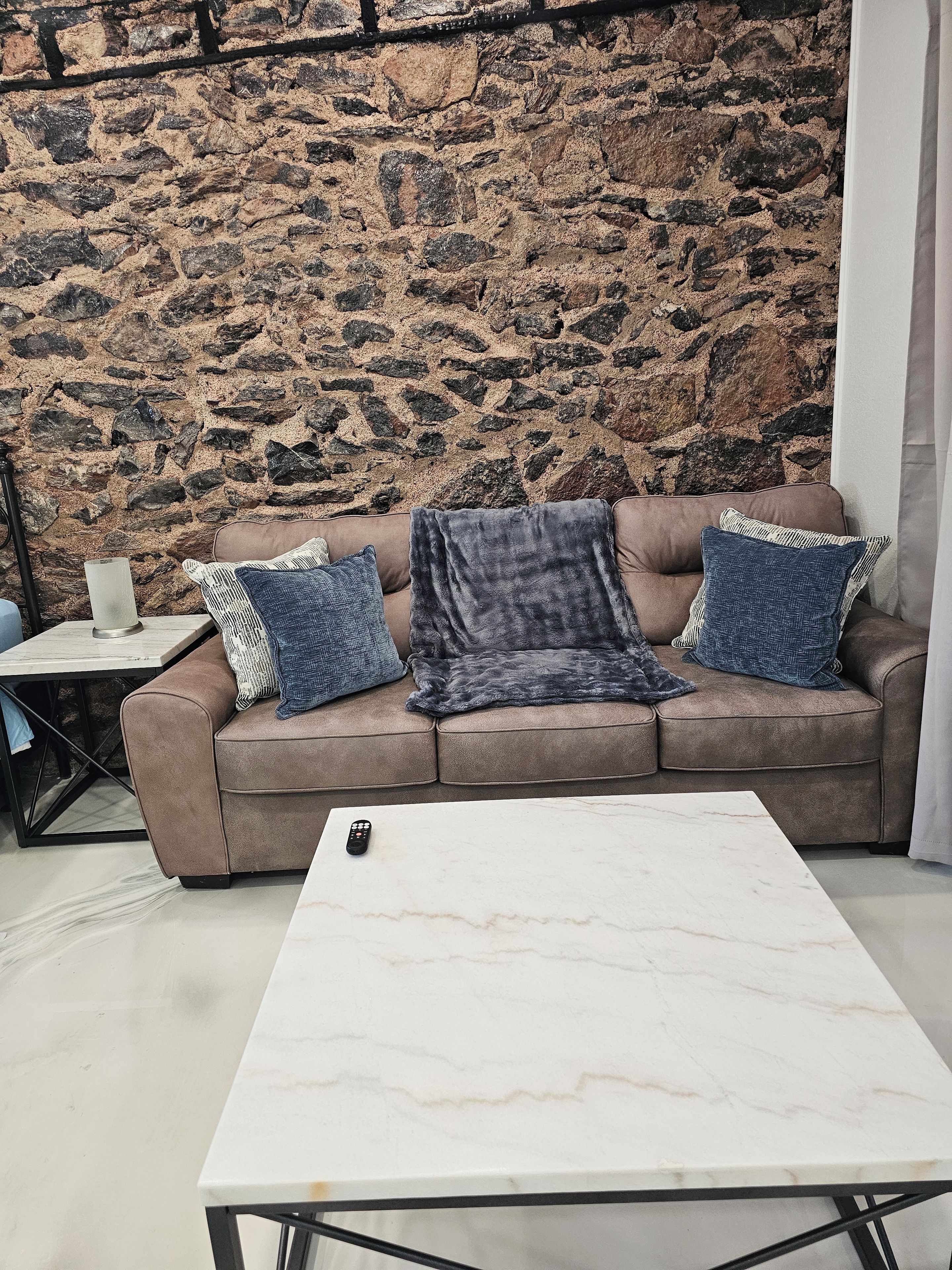 A living room with a stone wall, a brown sofa, and a marble coffee table.