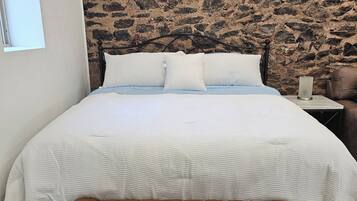 A bedroom with a stone-patterned headboard, a bed with white bedding, a bench at the foot of the bed, and a nightstand with a lamp.