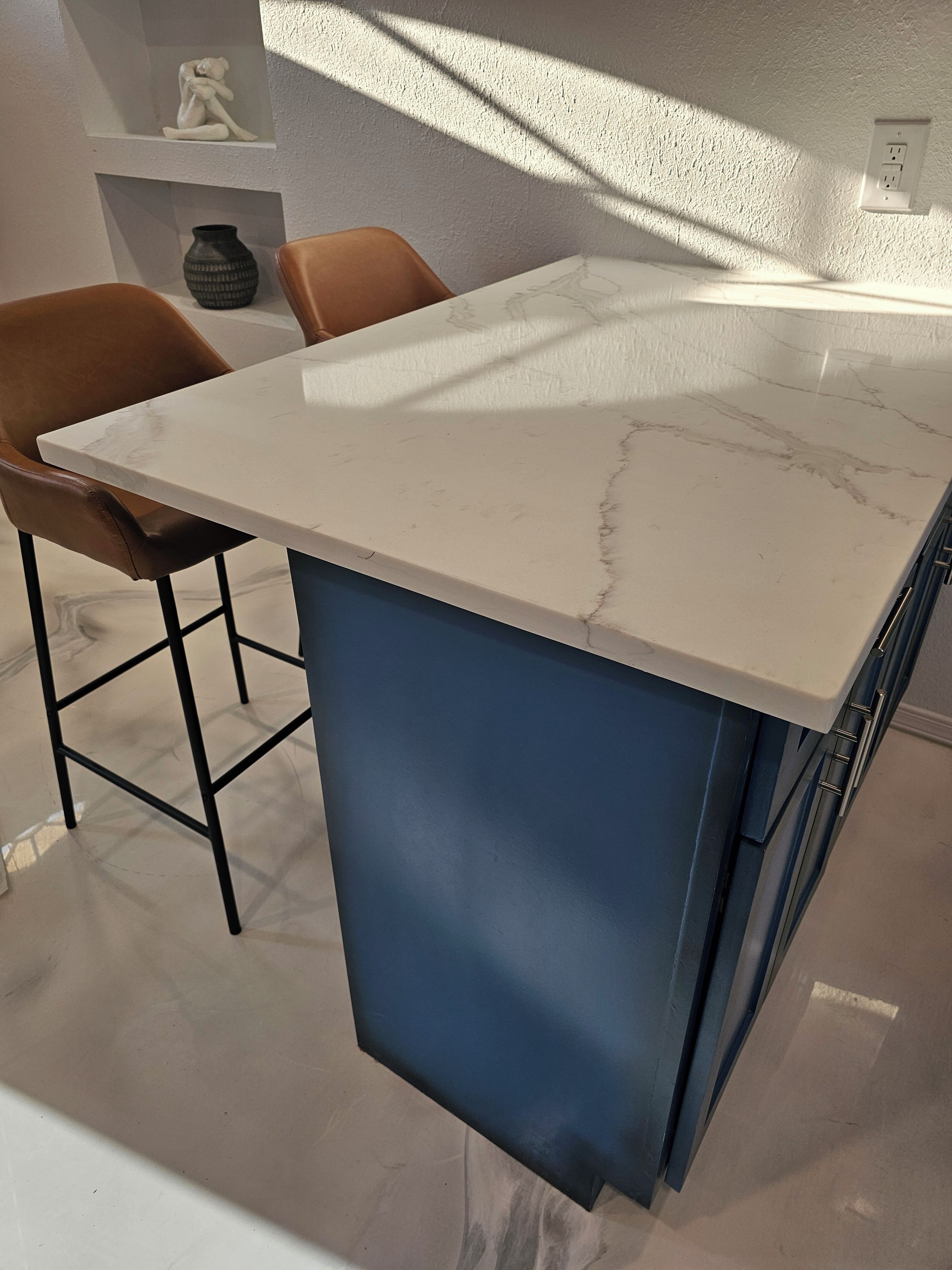 Una cocina con encimera de mármol, dos taburetes de bar y un armario azul.