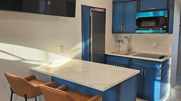 A modern kitchen with a central island, bar stools, a built-in oven, and blue cabinetry.