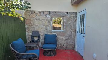 A patio with wicker chairs and a small window, a door, and a stone wall.