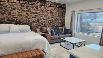 A modern bedroom with a stone wall, a bed, a sofa, and a view of the outdoors.