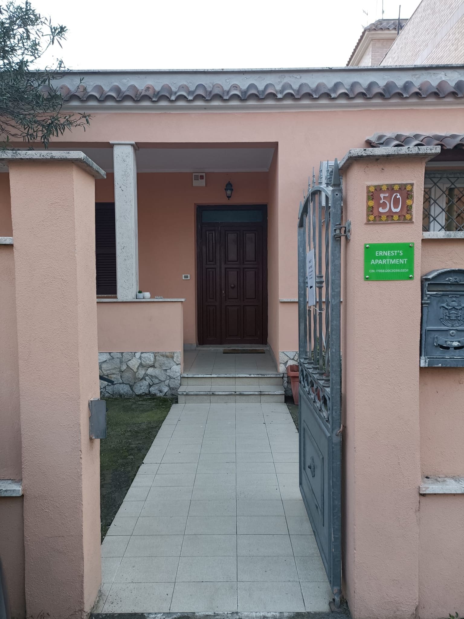 L'ingresso di un edificio con un vialetto lastricato che conduce a una porta, una cassetta delle lettere e un cartello che indica 'Ernest's Apartment'.