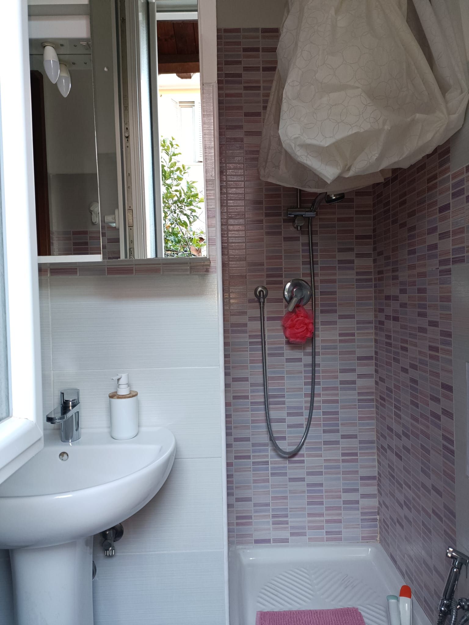 A bathroom with a white sink, a shower with a handheld showerhead, and a towel rack with a red towel.