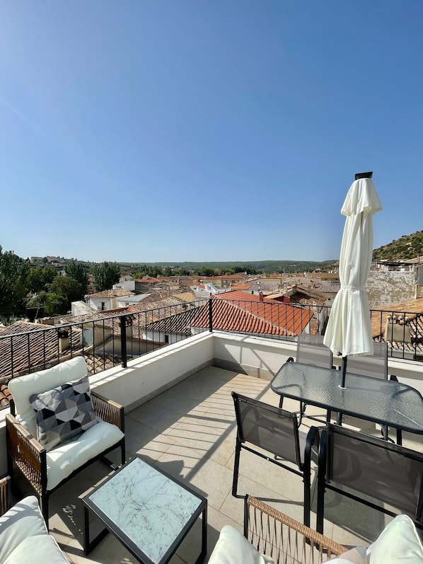 A rooftop terrace with outdoor furniture, a table, and an umbrella.