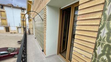 Un edificio residencial con fachada de tejas, un balcón con barandilla metálica y un automóvil estacionado en la entrada.