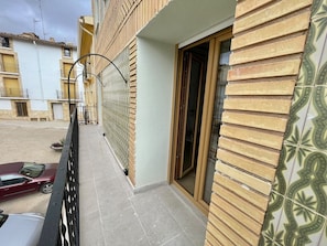 A residential building with a tiled exterior, a balcony with a metal railing, and a car parked in the driveway.