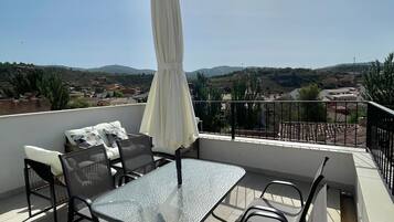 Una terraza en la azotea con una mesa, sillas y una sombrilla, y vistas al campo.
