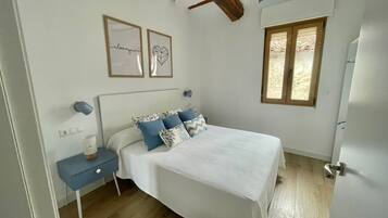 Un dormitorio con cama, mesitas de noche, ventana y techo con vigas a la vista.