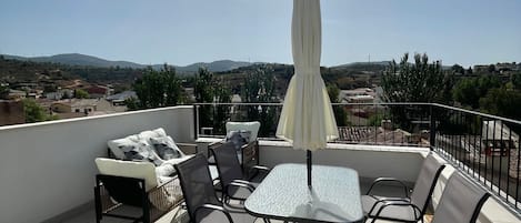 A rooftop terrace with a table and chairs, an umbrella, and a view of the landscape.