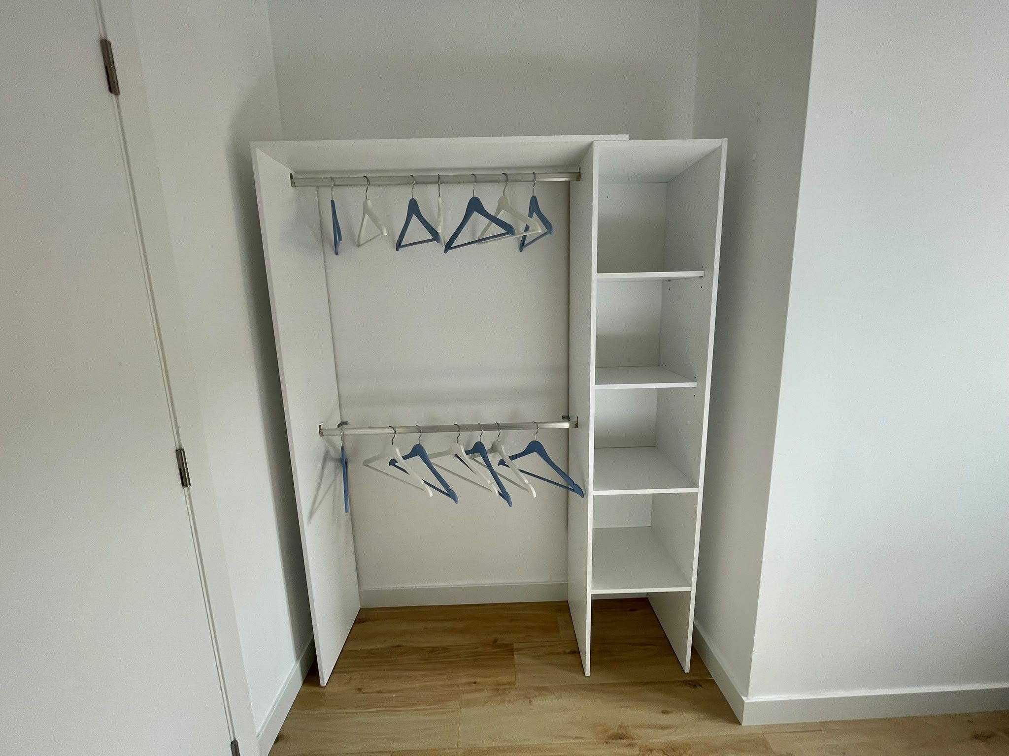 Un vestidor con piso de madera, paredes blancas y un armario blanco con estantes abiertos y espacio para colgar.