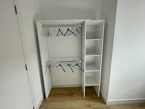 A walk-in closet with a wooden floor, white walls, and a white wardrobe with open shelves and hanging space.