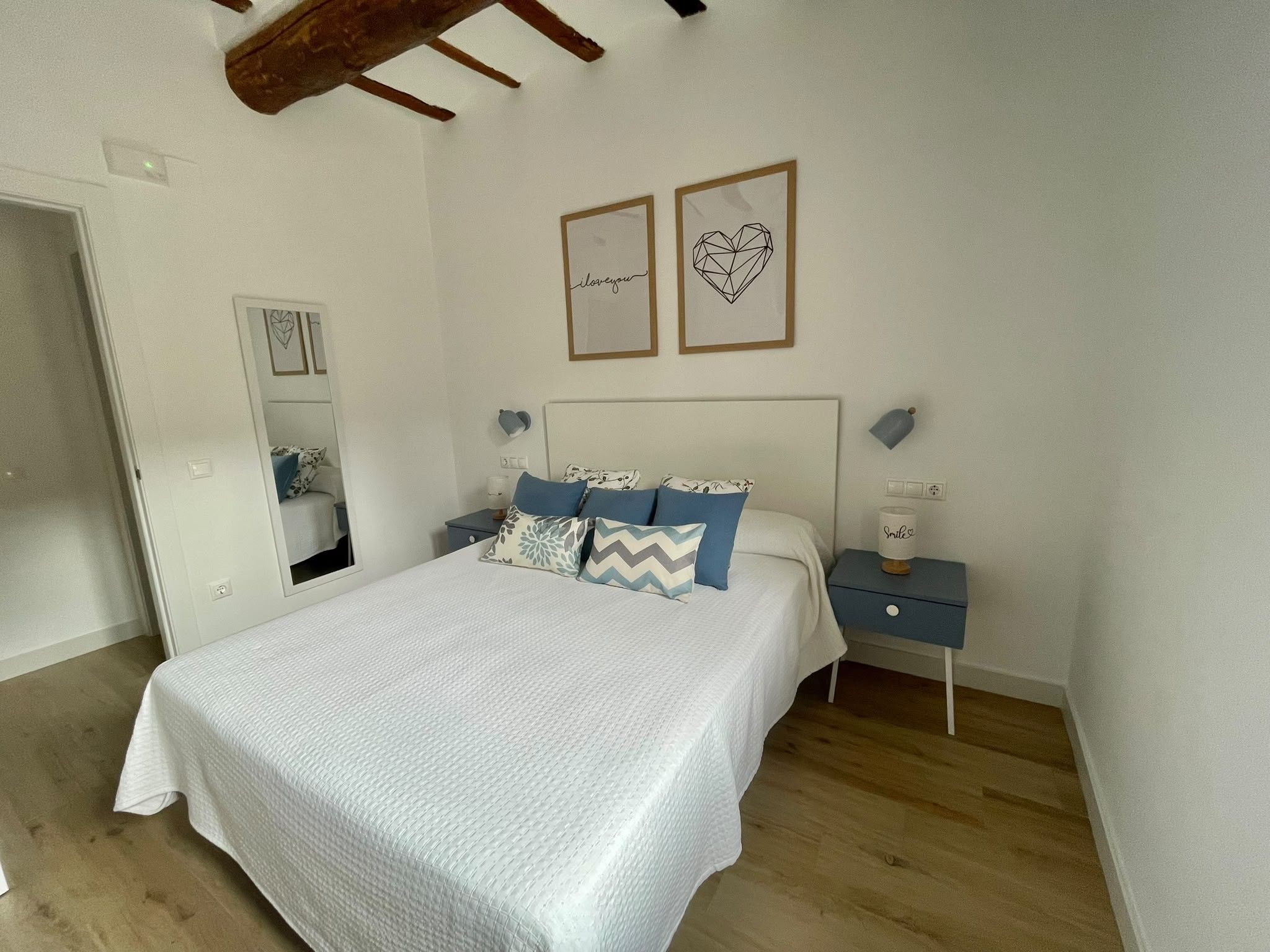 Een slaapkamer met een bed, een nachtkastje, een spiegel en twee foto's in lijsten aan de muur.