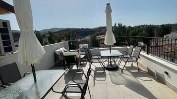 Un patio al aire libre con mesas y sillas, sombrillas blancas y vistas del paisaje.