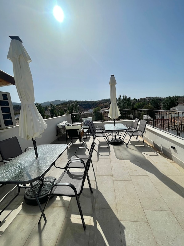 An outdoor patio with tables and chairs, white umbrellas, and a view of the landscape.